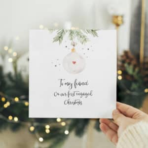 hand holding a christmas card for your first engaged christmas in front of green foliage