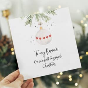 hand holding a christmas card for your first engaged christmas in front of green foliage